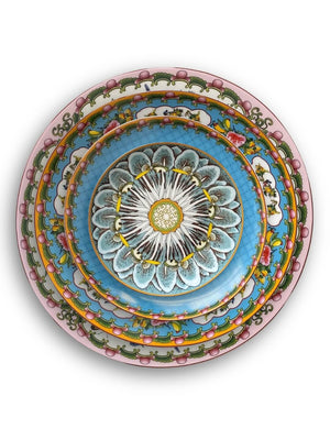 Stacked Paloma Plate Range tableware, showcasing pastel pink, green, yellow, blue, and white tones with floral, petal, and mandala-inspired patterns, viewed from above on a white background.