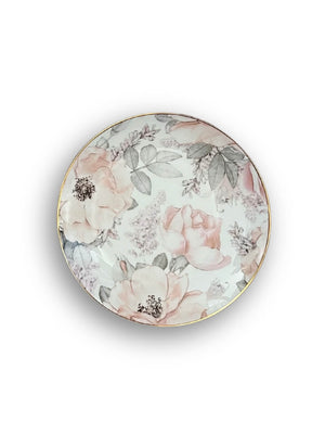 The Vera Plate Range showcases a round porcelain plate with a gold rim and delicate blush floral patterns—pink and white flowers with green leaves on a white background—perfect for elevating your garden-inspired tableware collection.