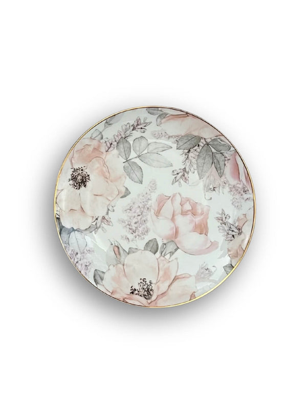 The Vera Plate Range showcases a round porcelain plate with a gold rim and delicate blush floral patterns—pink and white flowers with green leaves on a white background—perfect for elevating your garden-inspired tableware collection.