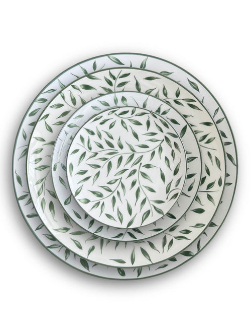 Four round white Willow Plate Range plates, each adorned with a green leaf motif, are stacked from largest to smallest and arranged concentrically on a white background, creating a fresh botanical look.