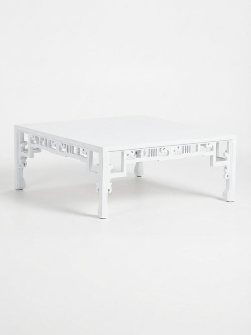The Bali Blanc Table is a modern coffee table with a high-gloss white finish, decorative cutout side patterns, and gently curved legs, showcasing Eastern-inspired design.