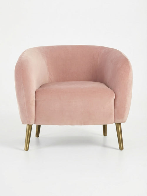 The Bellevue Chair is a blush pink velvet armchair with a curved back and seat, set on angled slender gold metal legs—a modern statement piece perfect for accenting any plain white background.