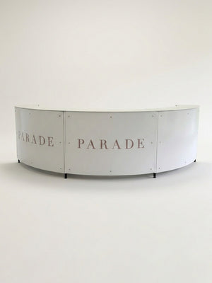 A curved, white Bespoke Branded Bar with PARADE in large light pink letters across its panels, set against a plain white background—ideal as an eye-catching corporate event bar.