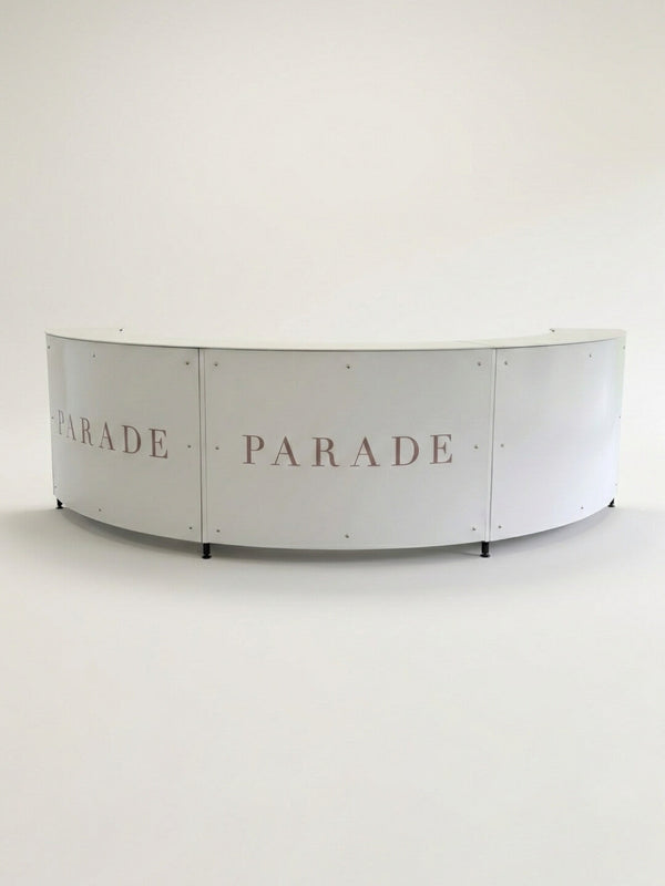 A curved, white Bespoke Branded Bar with PARADE in large light pink letters across its panels, set against a plain white background—ideal as an eye-catching corporate event bar.