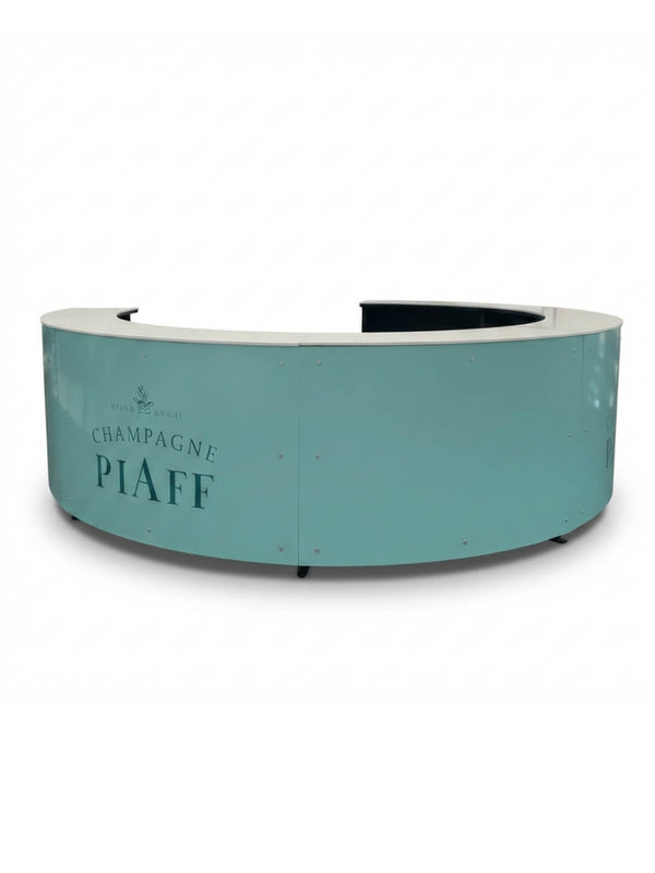 The Bespoke Branded Bar features a curved, light teal front with a Champagne Piaff and small crest logo, plus a white countertop. Its plain background makes it a versatile, customisable solution for events or receptions.