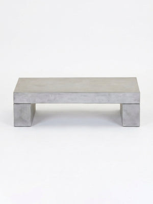 The Cementa Coffee Table features a minimalist, rectangular design with thick concrete legs for an industrial touch, showcased against a plain white background.