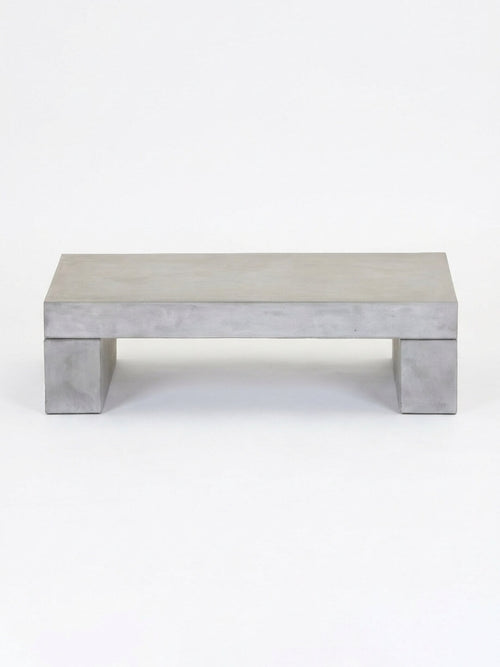 The Cementa Coffee Table features a minimalist, rectangular design with thick concrete legs for an industrial touch, showcased against a plain white background.
