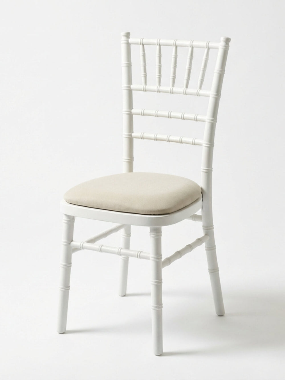 The Chiavari Chair - White features a spindle-style backrest and legs with a light beige cushioned seat, perfect for events. Custom seat pads are available for extra comfort. Shown against a plain white background.