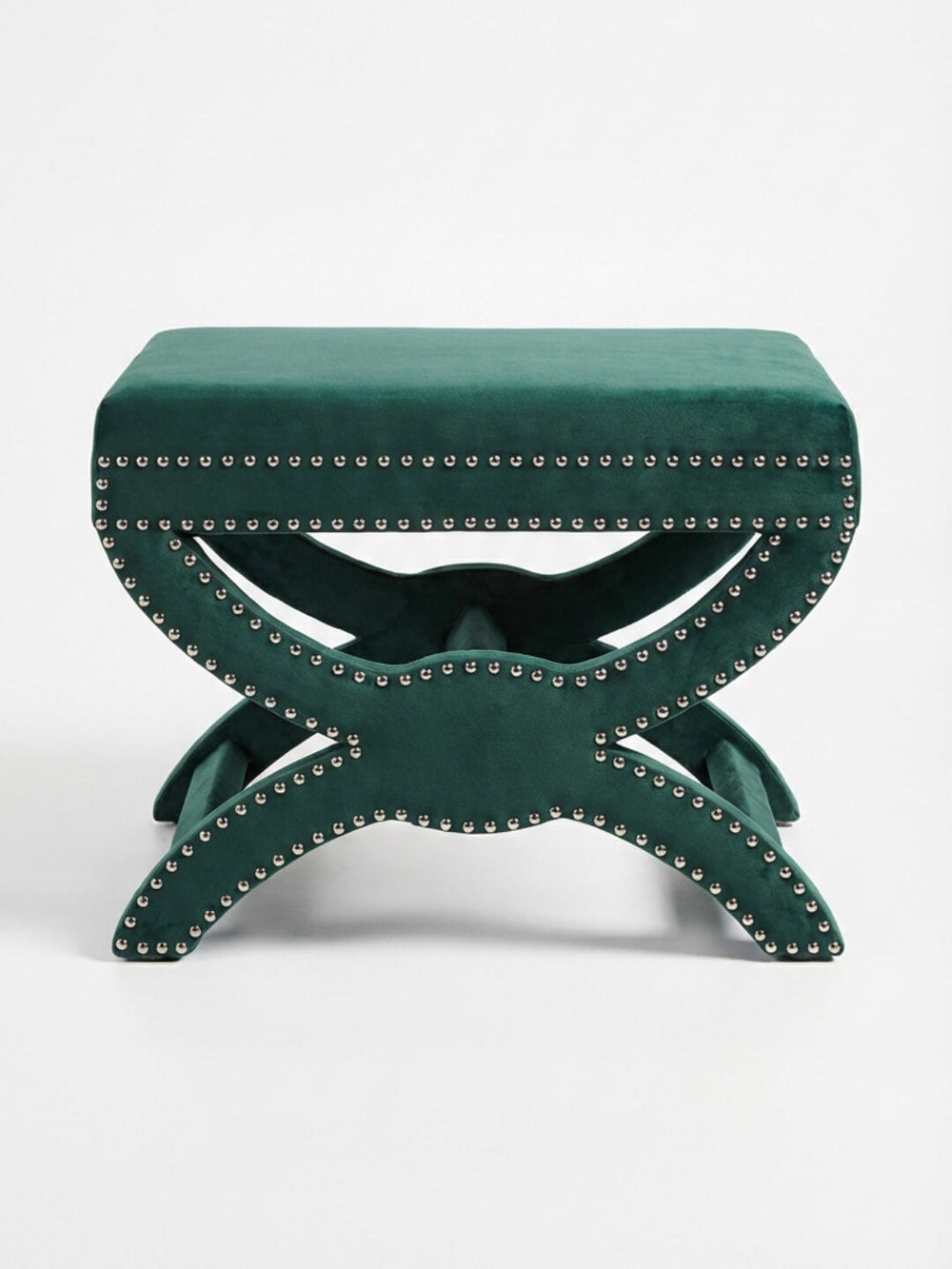 The Eden Stool features a green velvet rectangular cushioned top, silver nailhead trim, and a decorative X-shaped base, providing stylish statement seating against a plain white background.