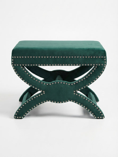 The Eden Stool features a green velvet rectangular cushioned top, silver nailhead trim, and a decorative X-shaped base, providing stylish statement seating against a plain white background.