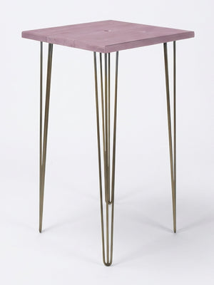 From the Hairpin Bar Table Collection, this minimalist side table has a square light purple wooden top and four slim gold hairpin legs—perfect as colorful event furniture against a plain white backdrop.