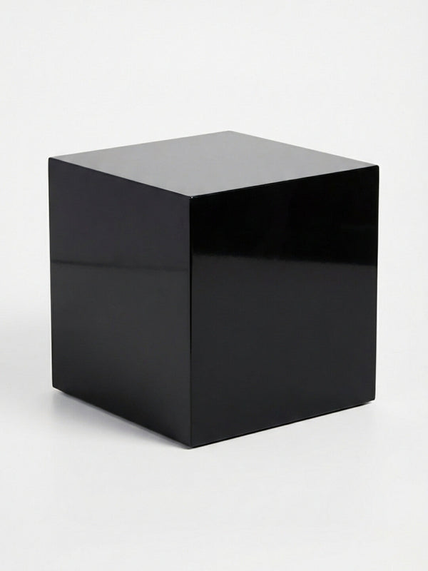 A sleek black cube from the Luxe Cube Collection rests on a white background, its glossy surface reflecting light—an elegant piece of event furniture.