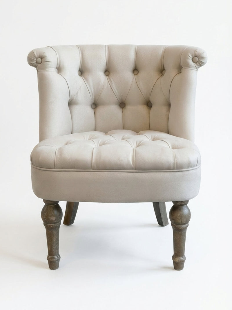 The Maison Chair features a beige tufted seat, wooden legs, rolled backrest edges, and button details for vintage charm and French elegance, shown against a plain white background.