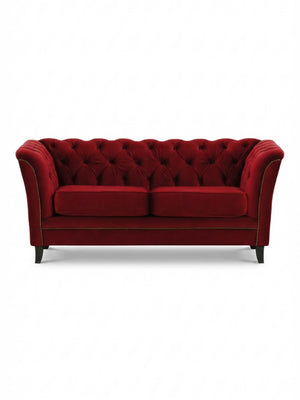 The Merlot Sofa is a luxurious red velvet piece featuring a tufted backrest, flared arms, gold nailhead trim, and four dark wooden legs for a vintage glamour look.