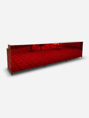 The Mirror Bar, a long rectangular piece with glossy red reflective surfaces, stands on a plain white background, partially reflecting its surroundings.