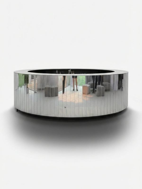 The Mirror Bar, a large circular bar sculpture with a plain white background, elegantly reflects outdoor scenes—grass, pavement, and blurred figures—while offering customizable options for modern events.
