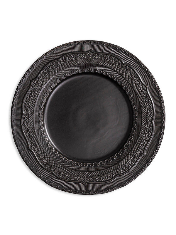 The Noir Charger Plate is a round, dark ceramic plate featuring a glossy finish and intricate raised patterns on its wide rim, ideal for luxurious tablescapes.