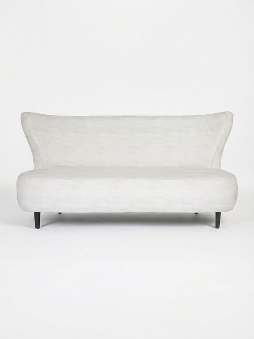 The Pearl Sofa is a modern, minimalist lounge piece in light gray with a curved backrest and short black legs, shown against a plain white background.
