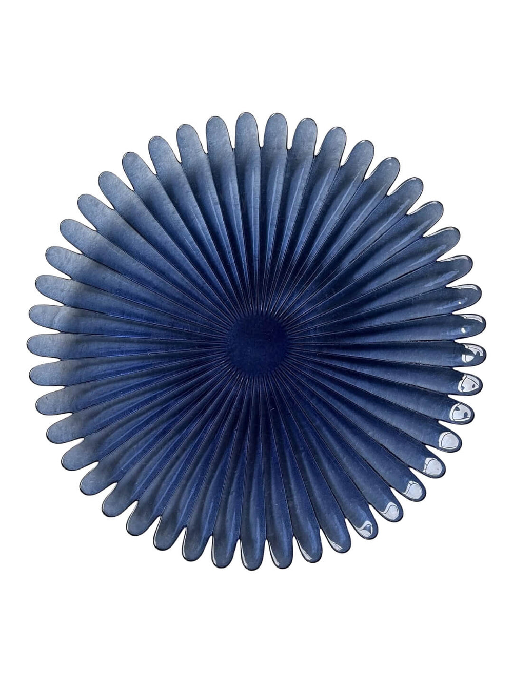 The Petra Blue Charger Plate is round and dark blue with petal-like ridges and a textured center, resembling a stylized flower or fan, displayed on a white background.