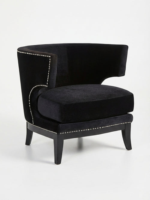 The Regent Noir Chair is a modern black velvet chair with a curved backrest, silver nailhead trim, and dark wooden legs—an elegant choice for contemporary events, shown here against a plain white background.