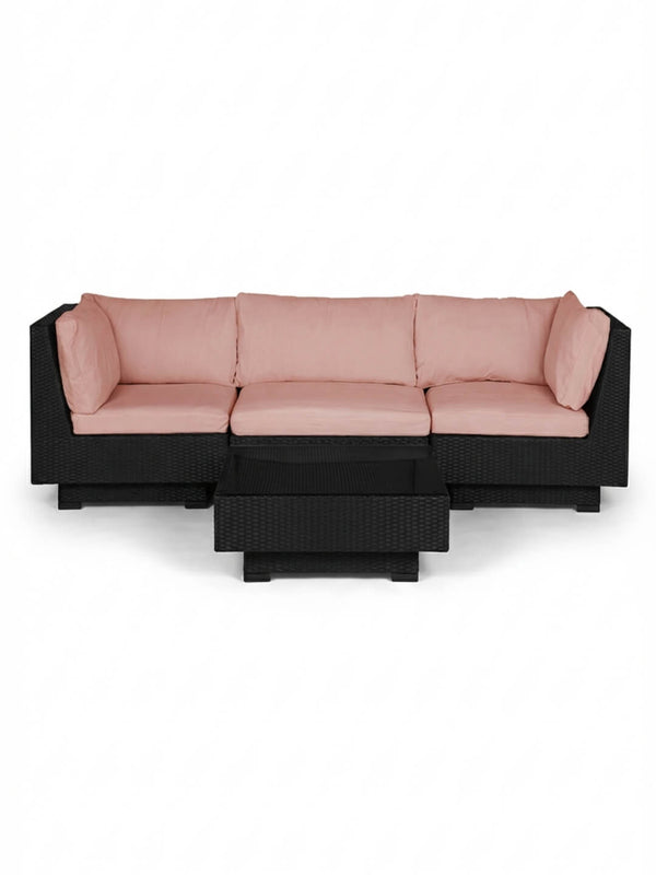 The Sereno Black modular outdoor rattan sofa with light pink cushions is arranged in an L-shape beside a matching low rectangular coffee table, forming a contemporary set against a plain white background.