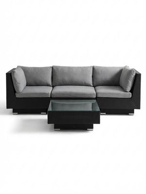 The Sereno Black set features an L-shaped black modular sofa with gray cushions and a matching black wicker coffee table with a glass top, all displayed against a white background.