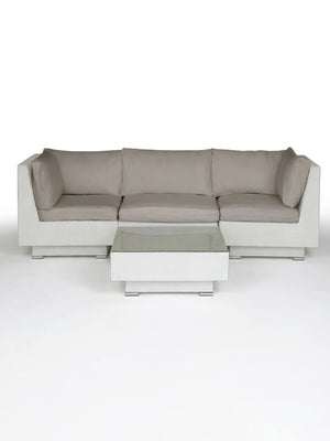 The Sereno White is a modern white rattan sectional sofa with light gray cushions and a matching square coffee table, perfect as outdoor lounge furniture, shown on a plain white background.