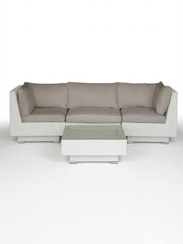 The Sereno White is a modern white rattan sectional sofa with light gray cushions and a matching square coffee table, perfect as outdoor lounge furniture, shown on a plain white background.