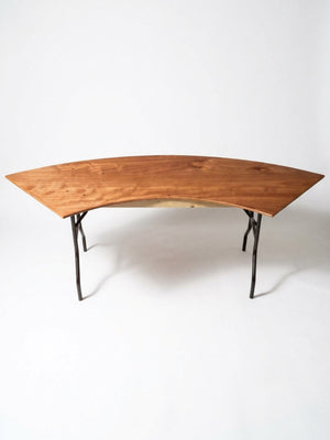 The Serpentine Table features a modern, curved design with a smooth natural finish and angled metal legs, shown against a plain white background.