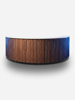 The Wood Bark Bar is a curved wooden reception desk with a textured front panel inspired by tree bark and a smooth, light-colored countertop, shown against a plain white background.