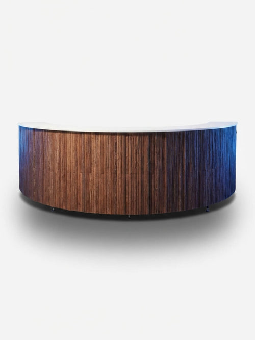 The Wood Bark Bar is a curved wooden reception desk with a textured front panel inspired by tree bark and a smooth, light-colored countertop, shown against a plain white background.