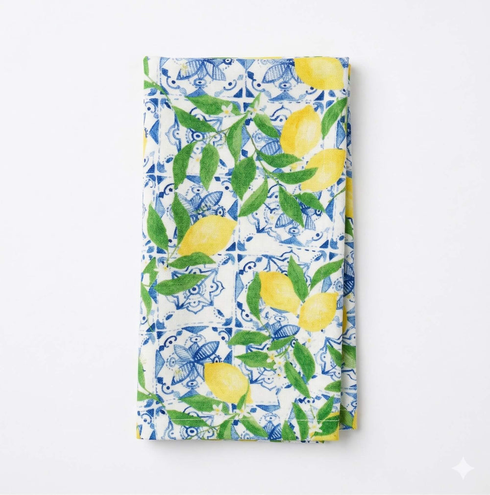 A close-up of the Elena Linen Sample, featuring yellow lemons and green leaves atop a blue and white tile motif, adds vibrant elegance and Mediterranean charm to any table.