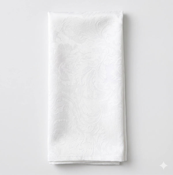 The Evie Linen napkin, neatly folded, features a subtle and elegant white floral damask pattern and is displayed on a plain light background.