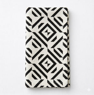 A Harper Linen cloth napkin, folded and white, showcases a bold black geometric pattern of diamonds and lines against a plain white background.