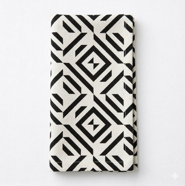 A Harper Linen cloth napkin, folded and white, showcases a bold black geometric pattern of diamonds and lines against a plain white background.