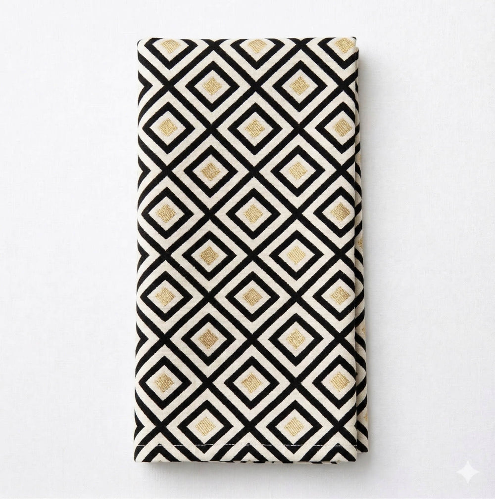 A close-up of a table with the Hera Linen Sample, showcasing black lines and gold squares on white fabric—ideal for luxury event decor, with soft folds draping elegantly over the edge.