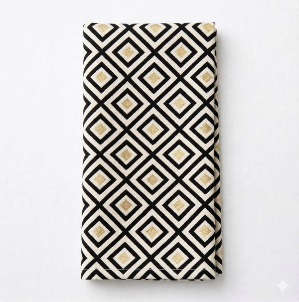 The Hera Linen napkin features a geometric black diamond pattern outlined in white with gold square accents on a white background—ideal for modern event decor and pairing with black and gold linens.
