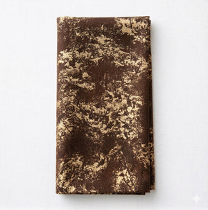 The Isabella Coffee Linen napkin features a neatly folded brown fabric with a beige, abstract marbled design, displayed on a white surface—perfect for elegant table settings and luxury event decor.