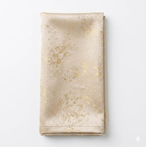 The Isabella Gold Linen napkin features a folded beige design with a subtle shiny gold marbled pattern, set on a white background—ideal for glamorous events and luxurious table settings.