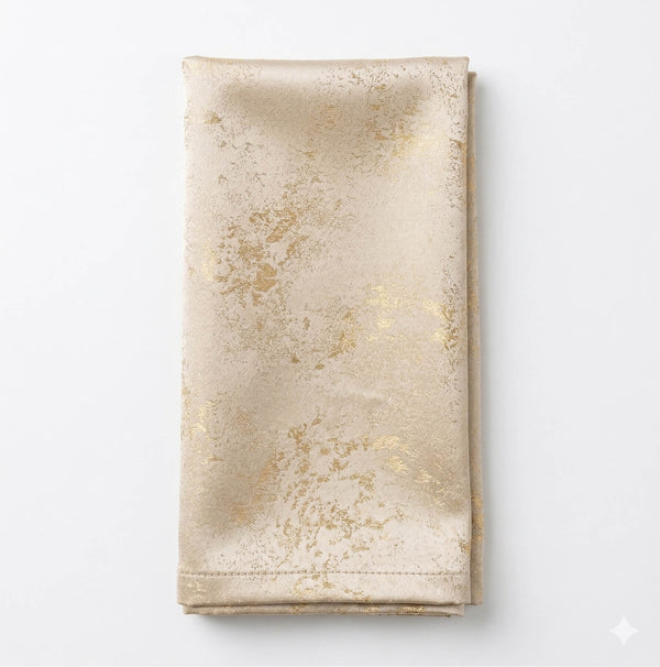 The Isabella Gold Linen napkin features a folded beige design with a subtle shiny gold marbled pattern, set on a white background—ideal for glamorous events and luxurious table settings.