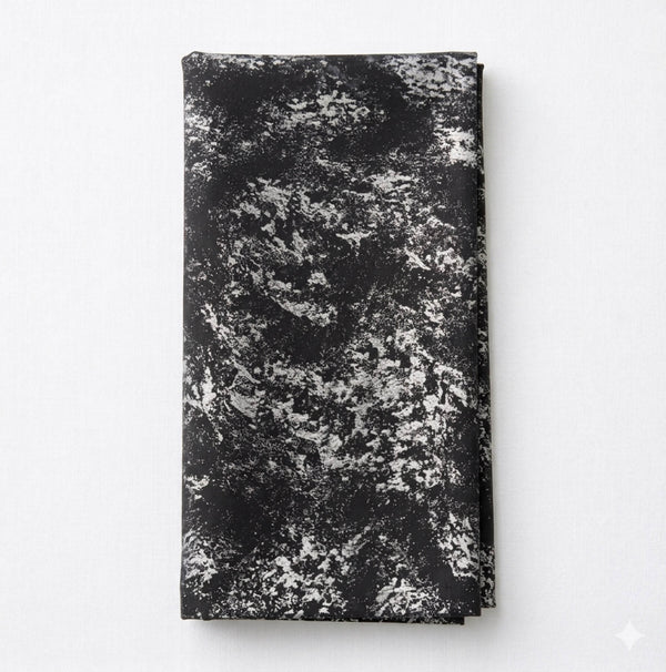 The Isabella Steel Linen, a folded black cloth featuring a textured abstract white and gray pattern, sits on a plain white surface—a striking piece of contemporary table linen.