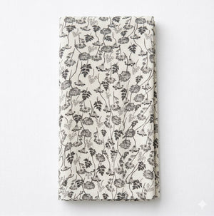 The Isla Linen beige fabric napkin features elegant black floral and vine patterns, shown folded against a white background.