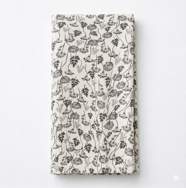 The Isla Linen beige fabric napkin features elegant black floral and vine patterns, shown folded against a white background.