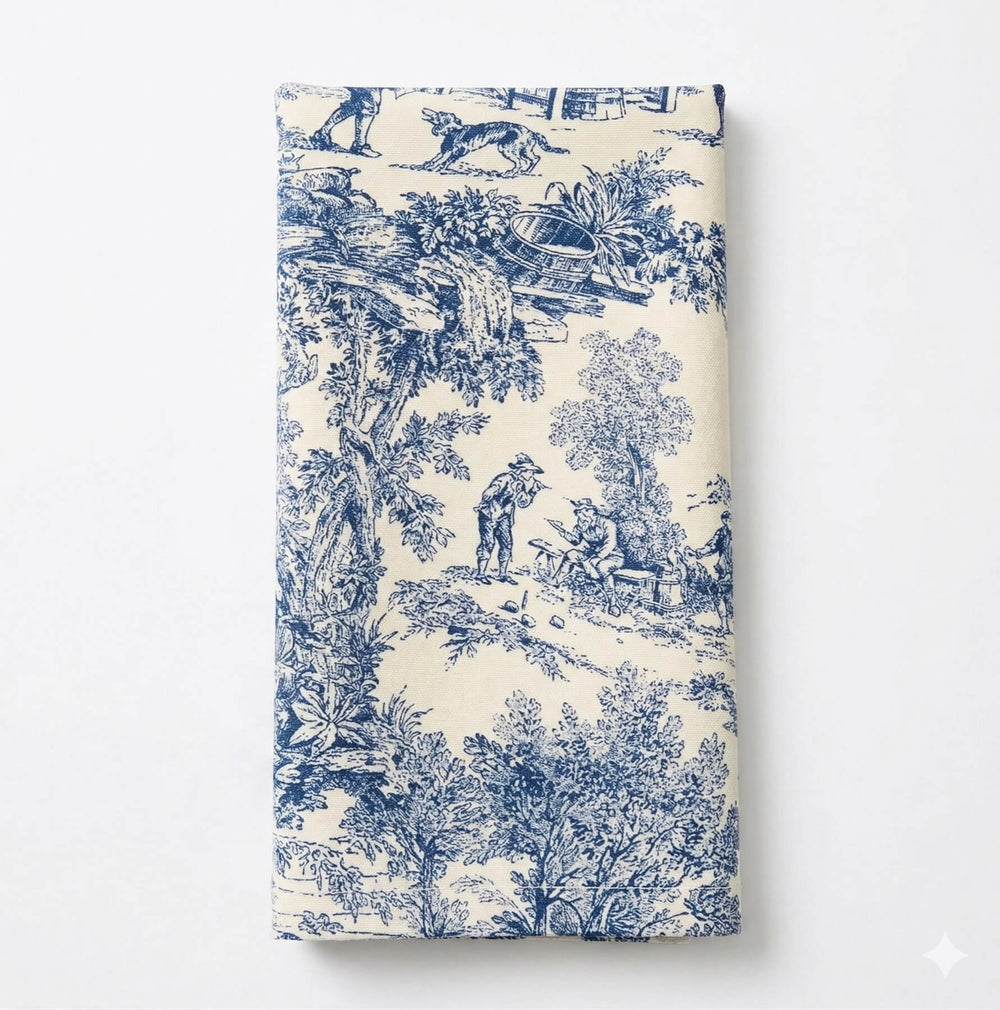 Close-up of Jolie Bleau Linen draped over a surface, showcasing detailed blue pastoral scenes with people, trees, and buildings—a perfect accent for timeless style décor.