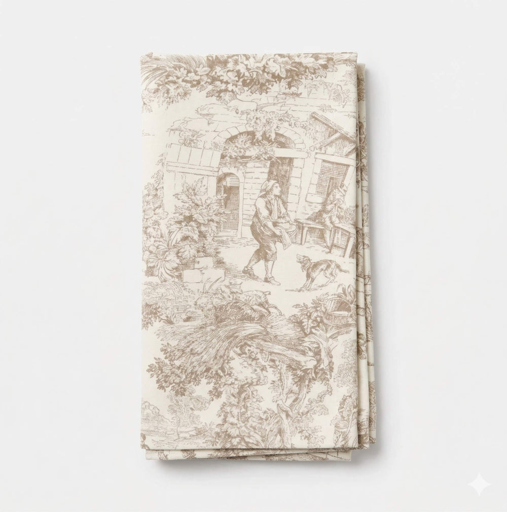 A close-up of Jolie Marron Linen showcases beige toile fabric with detailed brown pastoral scenes, including people, trees, and buildings—ideal for adding classic charm to any event setting.