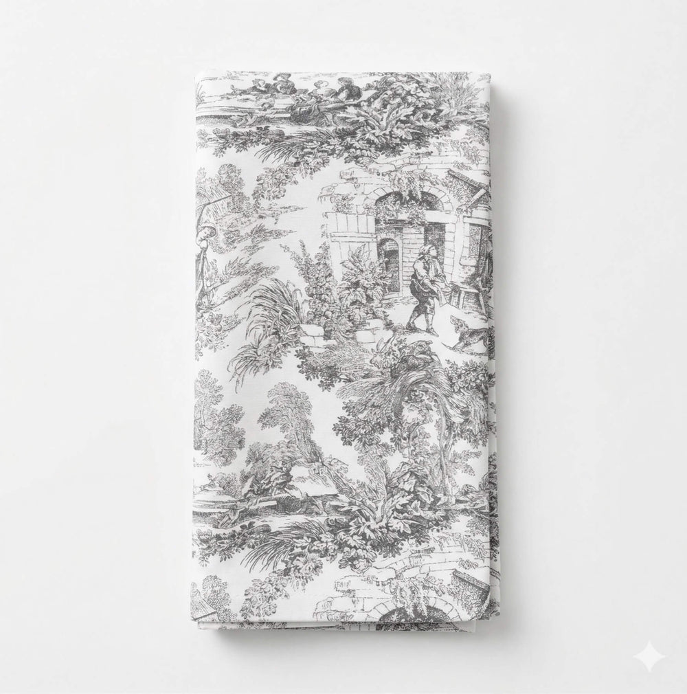 A close-up of the Jolie Noir Linen Sample reveals a detailed black-and-white pastoral scene featuring people, trees, and buildings in classic toile de Jouy style—part of an exclusive linen collection.