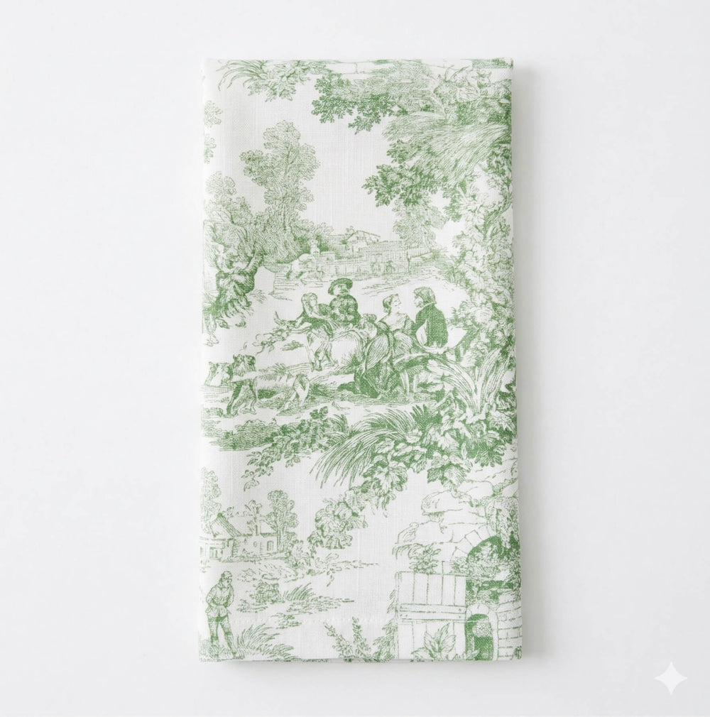 A close-up of the Jolie Vert Linen Sample shows its elegant green pastoral toile pattern with detailed garden scenes, softly draping over the table's edge.