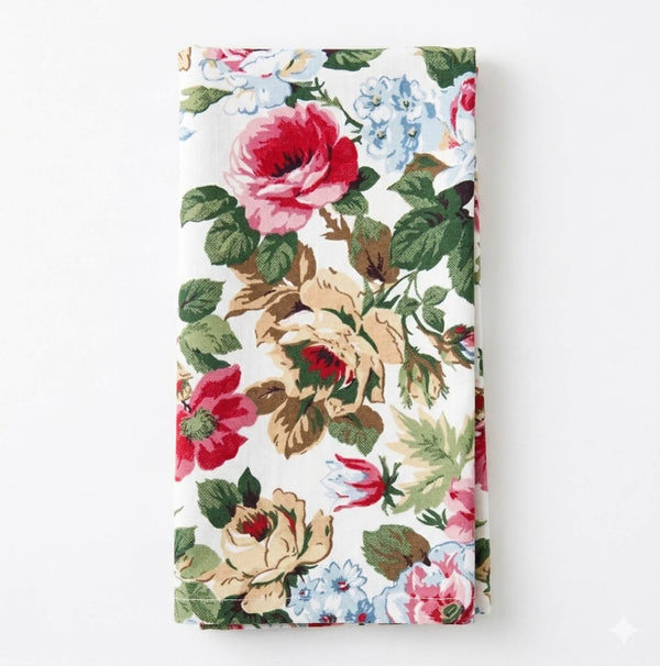 The Juliette Linen is a neatly folded fabric napkin adorned with romantic red, pink, blue, and beige florals with green leaves on a white background.