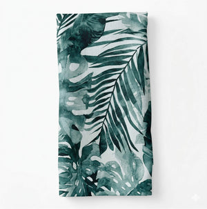 Layla Linen is a folded napkin with large, overlapping tropical leaves in varying green shades on a white background—perfect for adding a fresh touch to your table or event decor.