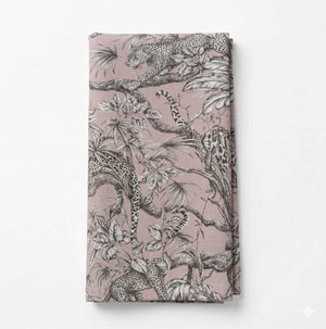 The Leonard Blush Linen, folded and shown on a plain white surface, features black-and-white leopard and jungle motifs on a vintage pink background.